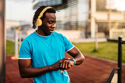 Athlete check fitness tracker on smartwatch or playing his music playlist after working out in outdoors gym.