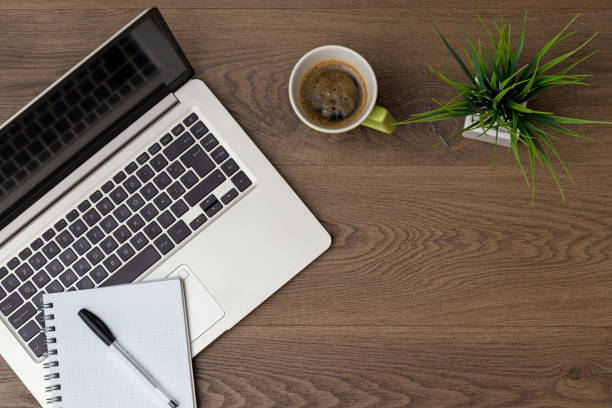 istock Top view of workspace. Table desk with laptop, coffee, notepad, pen and plant with empty space background for design. Flat lay view of dark brown wooden desktop. 1319094655