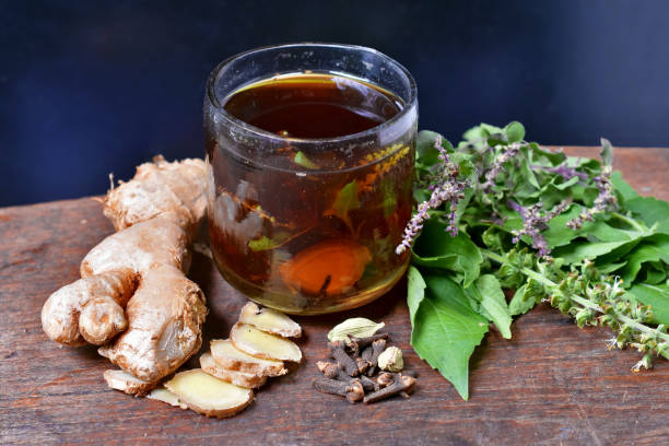 ingredients in a small glass of herbal tea ingredients are ginger, basil, cardamom, cloves on wooden table with black background - cardamom plant spice green imagens e fotografias de stock