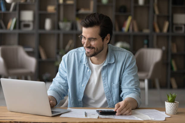 istock Smiling businessman in glasses using laptop, calculating bills, managing finances 1319095694