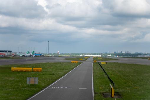 a taxi lane leading to a main runway at the airport of Schiphol in the Netherlands. Passenger planes can be seen parked at the terminals in the background