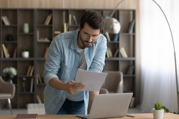 istock Confident businessman in glasses reading document, standing at work desk 1319095986