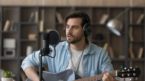 Photo of Close up man in headphones playing guitar, singing in microphone