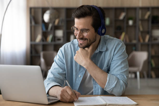 istock Close up smiling man in headphones using laptop, taking notes 1319096236
