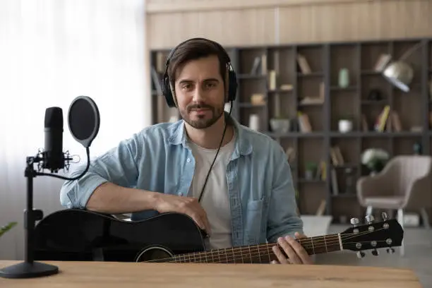 Photo of Portrait man in headphones holding guitar, sitting in home studio