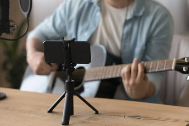 istock Close up smartphone on tripod, man playing guitar, recording video 1319096256
