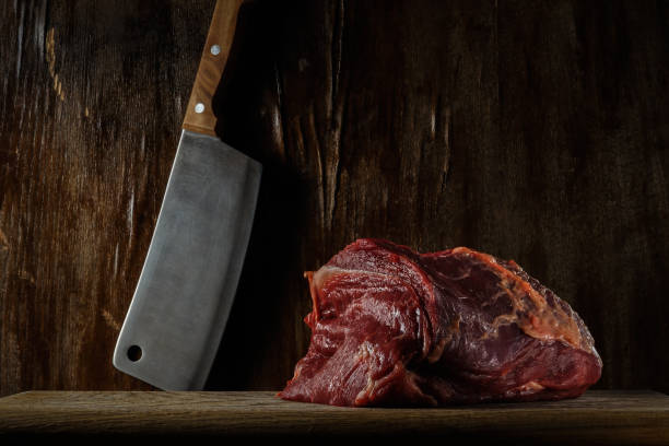 trozo de carne cruda fresca en una tabla de cortar con una cuchilla de cocina cerca de una antigua pared de madera. foto artística malhumorada en estilo rústico con espacio de copia - veal meat raw steak fotografías e imágenes de stock