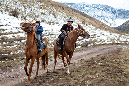 Bishkek, Kyrgyzstan - October 20, 2018: Nomadic father and his son ride horse near Bishkek, Kyrgyzstan