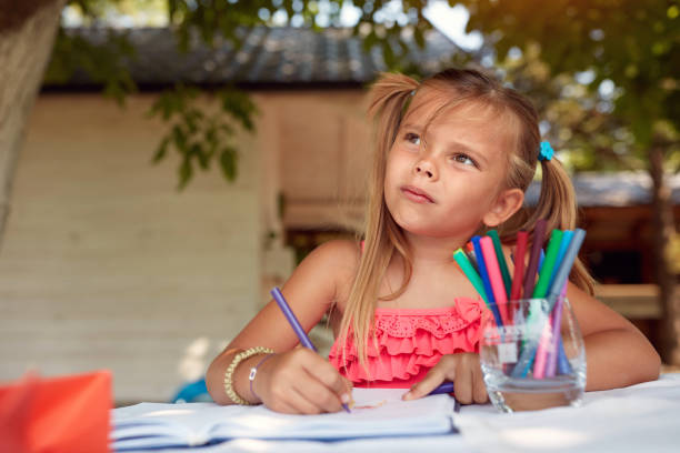 istock cute little girl thinking, looking up, while drawing with felt tip pen 1319097658