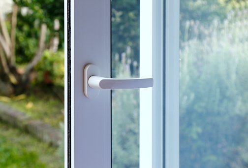 Open door of a family home. Close-up of the lock on the sliding door with the yard of background. White PVC door and double glass.
