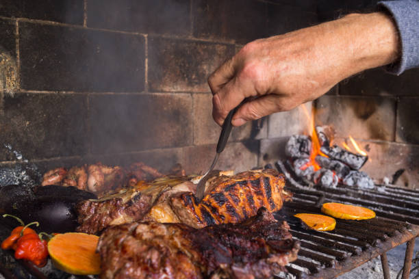 homme faisant le barbecue pour le déjeuner. coupes de viande et légumes chauffant sur les braises sur un gril de fer. barbecue argentin traditionnel. - steak argentina food silverware photos et images de collection