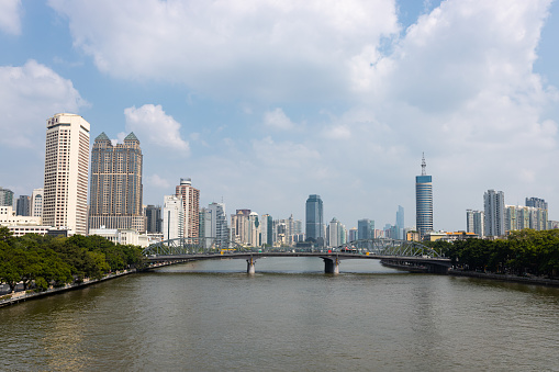 Guangzhou, China - November 11, 2019: A bridge across the river on the banks of which there are park areas. In the background are skyscrapers and high-rise buildings. China, Guangzhou