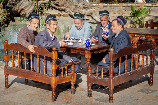 Bukhara, Uzbekistan - October 14, 2018: Group of Uzbek men wearing traditional hats drink tea in Bukhara, Uzbekistan