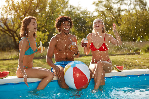 afro-american young man having fun with two caucasian females outdoor by the pool afro-american young man having fun with two caucasian females outdoor in the nature by the pool black man eating watermelon stock pictures, royalty-free photos & images