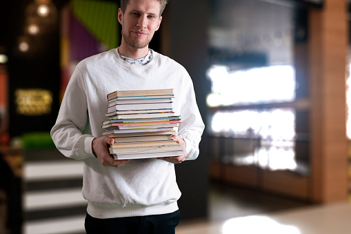 student holding stack of books, carry heavy paper textbooks, motivation concept