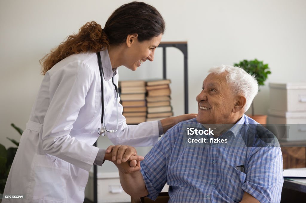 Thankful mature sick man holding nurse hand appreciating for help Thank you doctor. Smiling thankful mature sick man holding young female medic nurse hand appreciating for help support care. Happy woman gp greeting old man patient with recovery good analyses results Doctor Stock Photo