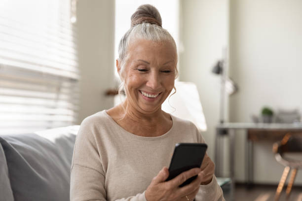 istock Smiling senior female use mobile phone app enjoy playing game 1319103361