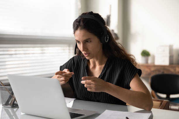 femelle concentrée dans le casque s’asseoir par pc support client à distance - translation photos et images de collection