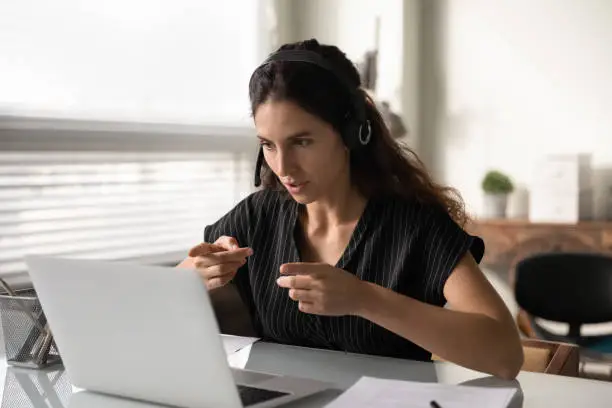 Distant consultation. Concentrated latin female in headset sit by pc support client remotely assist to solve technical problem. Focused young lady interpreter working online translating simultaneously
