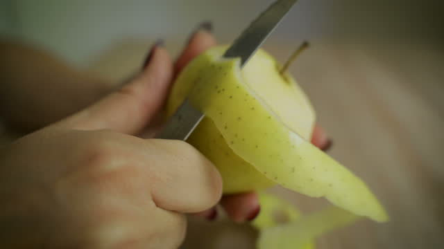 Hands peeling a green apple on a wooden board