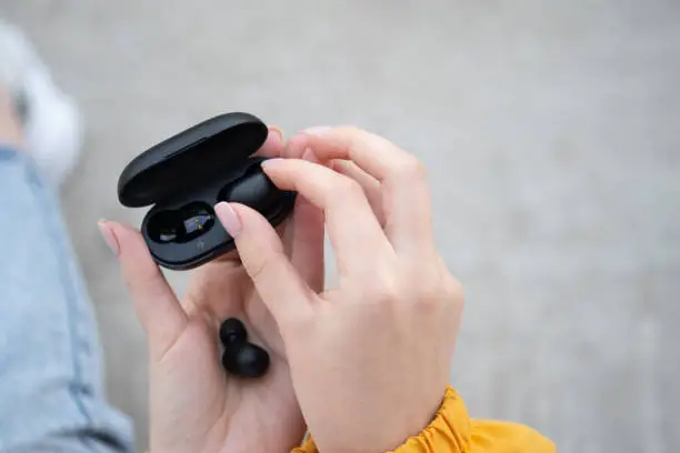 Photo of close-up of a woman taking out a black wireless earbud from his charging box. Female hands touching a portable gadget headphones. Bluetooth headset.