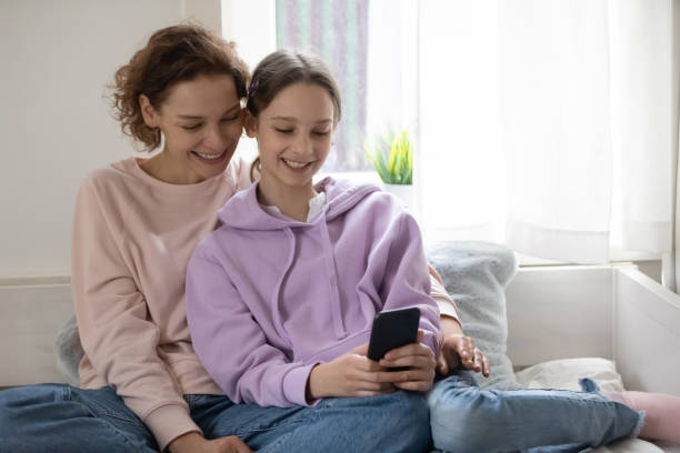 스마트 폰 응용 프로그램을 사용하여 미소 어머니와 십대 딸. - adoption early teens teenager family 뉴스 사진 이미지