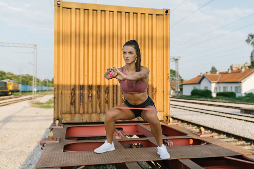 Portrait of a young fit woman doing squats outdoor with a resistant band