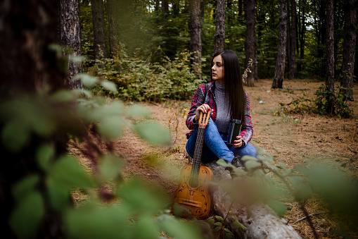 A happy woman enjoys nature, sits in a forest with tall trees, leads a healthy lifestyle away from city noise. A young woman enjoys a beautiful spring day in nature - Eastern Serbia.