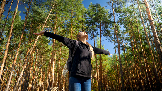 Portrait of smiling female tourist stretching hands and enjoying morning in pine tree forest,