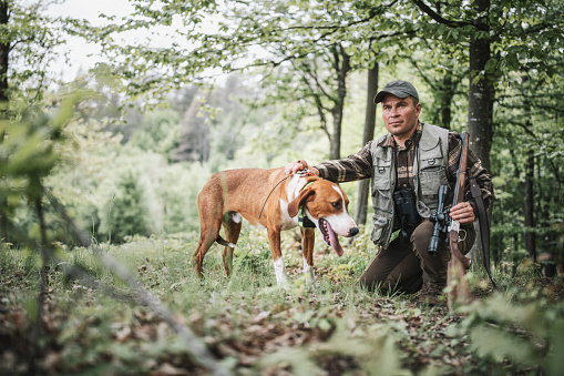 A shot of huner and dog waiting in the forest.