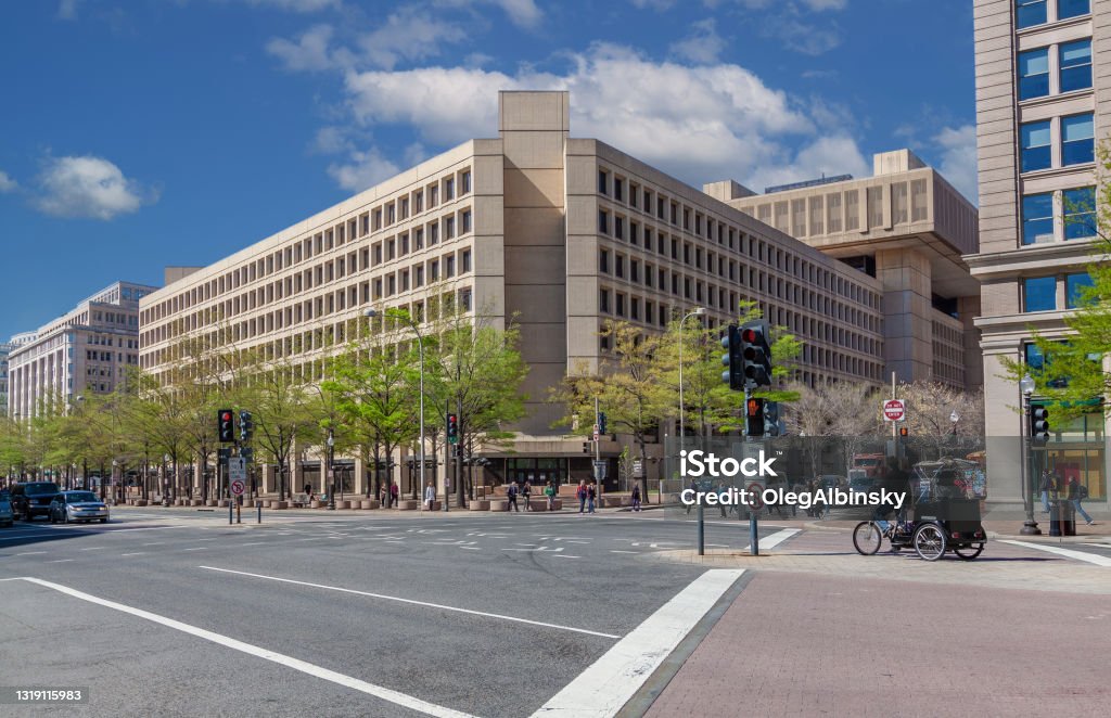 Federal Bureau of Investigation (FBI) Headquarters and Blue Sky with Puffy Clouds, Washington DC, USA. Federal Bureau of Investigation (FBI) Headquarters on Pennsylvania Avenue, Washington DC, USA. Blue Sky with Puffy clouds, Street, Rickshaw, Passersby and Green Trees are in the image. Wide angle lens. Washington DC Stock Photo