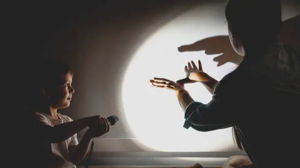 Photo of Toned photo of young mother and little boy playing in theater of shadows before going to sleep at night