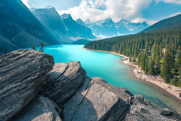 lago moraine en el parque nacional banff en un día de verano parcialmente nublado. cordillera en la parte posterior en una neblina suave. el viento persigue nubes a través del cielo. senderismo en las montañas rocosas canadienses. - moraine fotografías e imágenes de stock