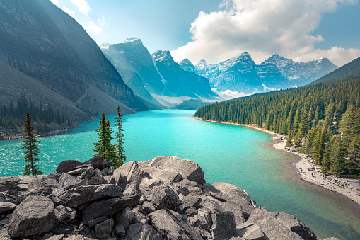 Moraine Lake in Banff National Park on a partly cloudy summer day. Mountain range in the back in a soft haze. Wind chases white clouds across the sky. Hiking in the Canadian Rockies.