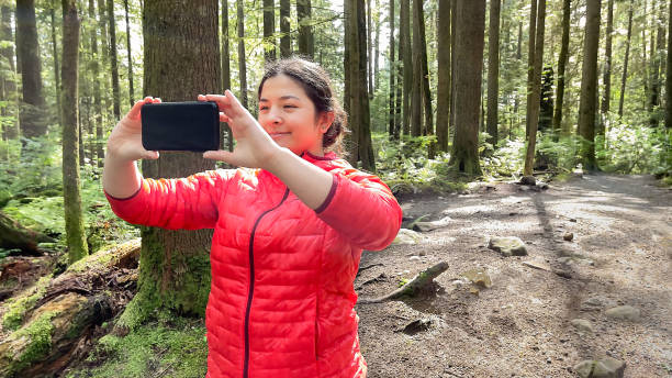 joven multiétnica tomando foto de teléfono inteligente en bosque iluminado por el sol - mt seymour provincial park fotografías e imágenes de stock