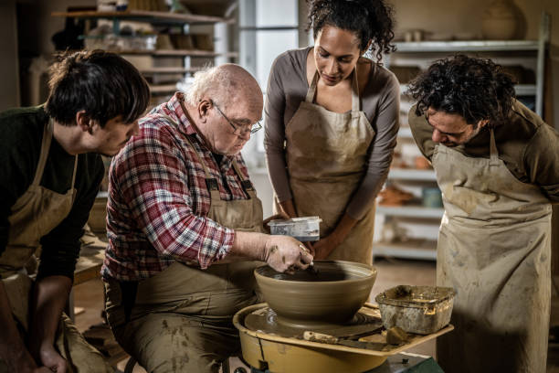 istock Master potter teaching his students how to sculpt a bowl on a spinning pottery wheel 1319131563