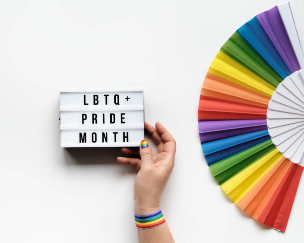 LGBTQ pride month decor. Text Happy Pride Month on lightbox. Rainbow pattern fan on off white background. Human hand with rainbow nail varnish holds light box. June, LGBT pride month pride symbols. decoración del mes del orgullo lgbtq. texto feliz mes del orgullo en lightbox. ventilador de patrón arco iris en el fondo blanco. la mano humana con barniz de uñas arco iris sostiene caja de luz. junio, decoración del orgullo del mes del orgullo lgbt