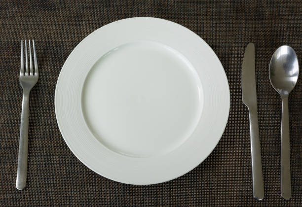 istock Close up and selective focus shot of tableware (white plate, fork, spoon and knife) on table in restaurant which is well prepared and decorated for lunch and dinner meal or food. 1319144273