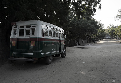 A solitary 60s bus is parked at the sand and quiet streets of Old Bagan in Myanmar. The rural atmosphere and the presence of vegetation does not resemble an urban space.