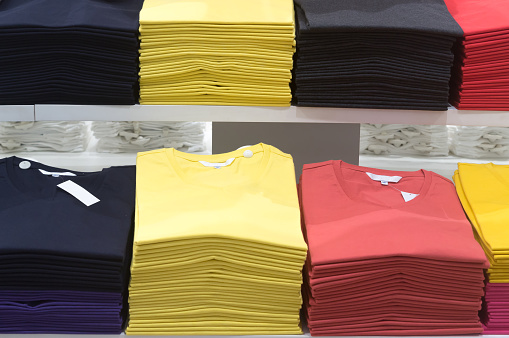 Multi colorful beautiful t-shirts are together in tidy stacks in department store.