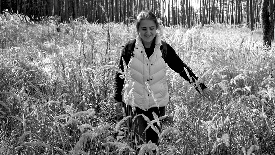 Black and white portrait of beautiful smiling woman walking through high dry grass in forest.