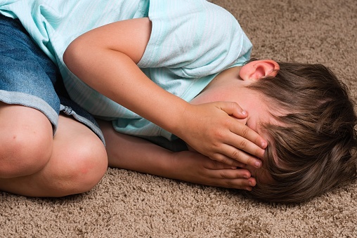 Caucasian little boy on the floor covering his face