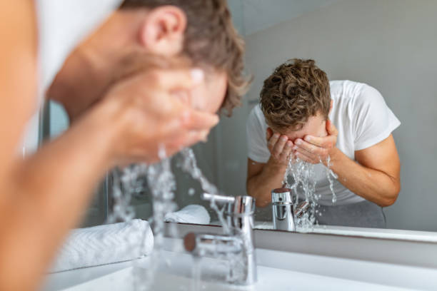 Face wash man splashing water cleaning washing face with facial soap in bathroom sink. Men taking care of skin, morning face wash routine for cleaning acne pimples stock photo