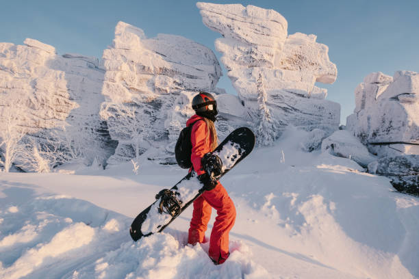 donna con snowboard su pista innevata soleggiata con splendida vista sulla valle delle rocce di montagna. stile di vita all'aperto sportivo, colori rosa tramonto - sheregesh foto e immagini stock