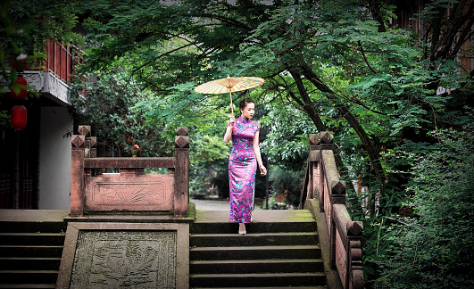A woman dressed in a cheongsam dress walked on an ancient stone bridge, holding an oiled paper umbrella