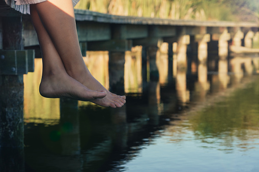 Woman's feet hanging down to the water on a wooden bridge. Inspirational concept