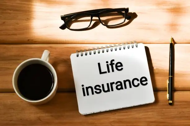 LIFE INSURANCE text written in a notepad near a cup coffee, eyeglasses and pen on a wooden background. Business concept. Flat lay