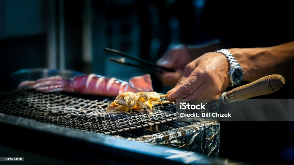 Grill Master An assortment of food is cooked on a grill by a street vendor on Enoshima Island in Japan. Animal Arm Stock Photo
