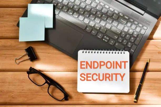Photo of ENDPOINT SECURITY inscription in a notepad near a laptop  and eyeglasses on a wooden background. Business concept. Flat lay.