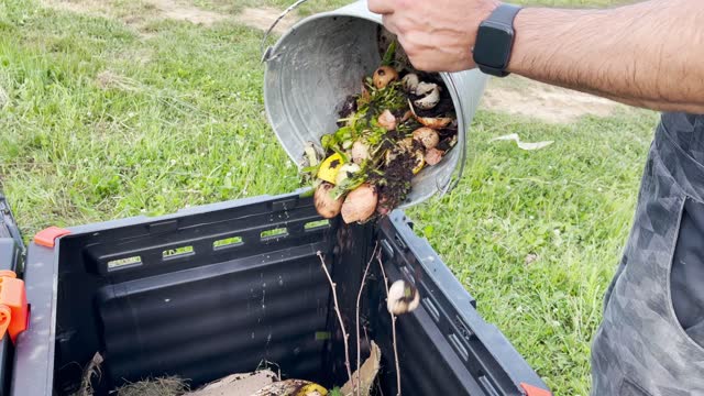 Man Emptying Organic Waste Bucket With Food Leftovers Into Composter